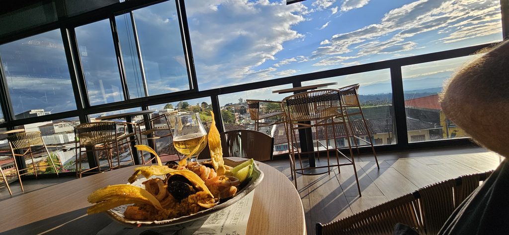 Seafood dish with fried plantains and beer served at a rooftop restaurant overlooking a scenic landscape during a Beyond The Ride cycling tour