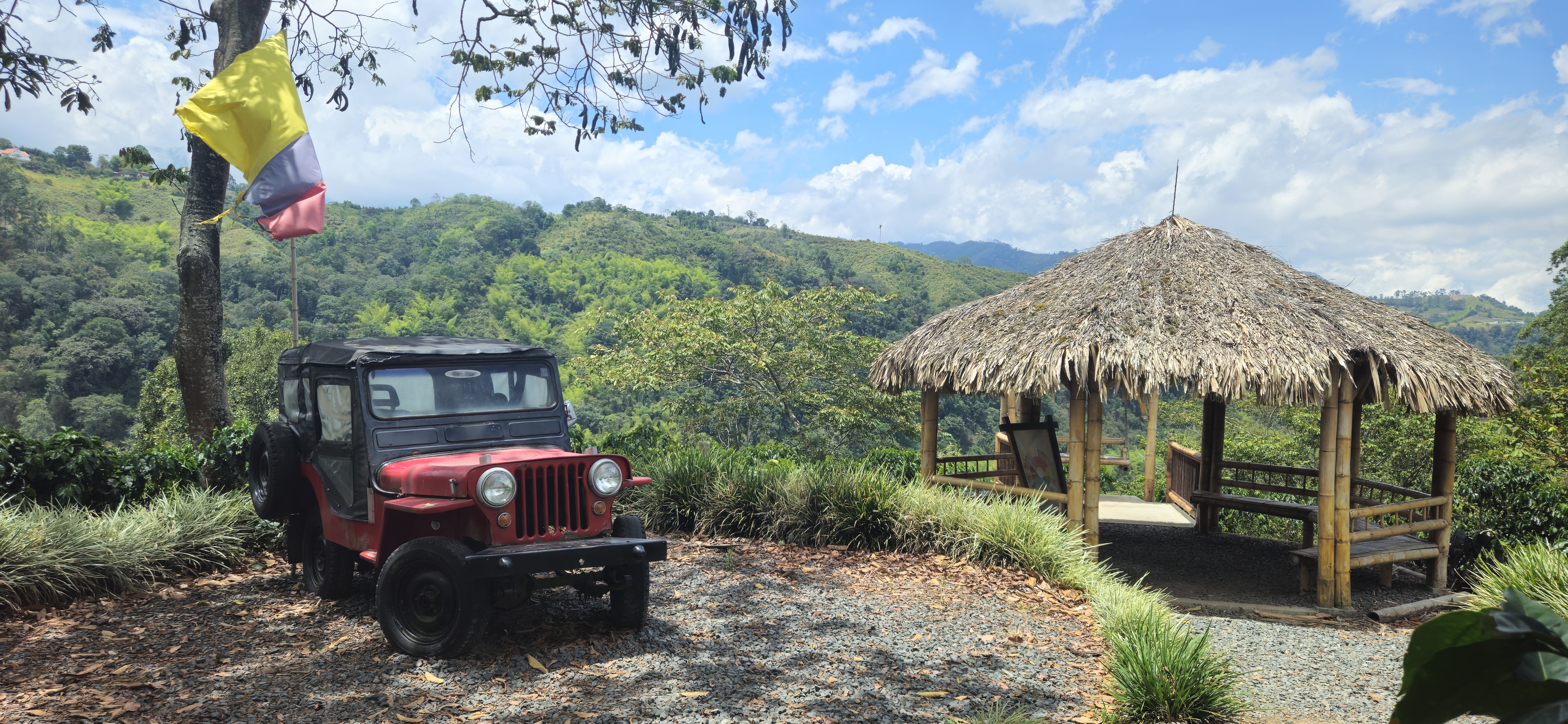 Red vintage Willys Jeep and thatched bamboo gazebo overlooking lush green mountains on a Beyond The Ride cycling tour in Colombia
