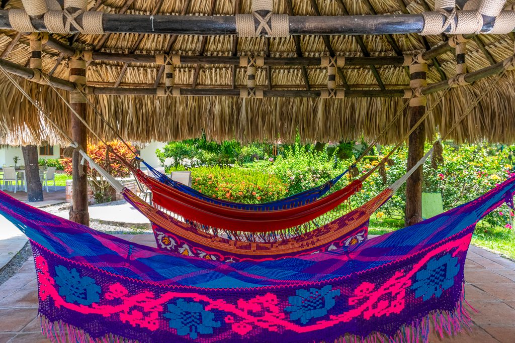 Colorful woven hammocks hanging under a thatched roof bamboo kiosk surrounded by lush green gardens at a boutique accommodation during a Beyond The Ride cycling tour